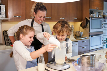 Happy cute siblings helping smiling mother to bake in kitchen