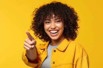Close-up portrait photography of a grinning girl in her 20s making an ok gesture with the fingers against a yellow background. With generative AI technology