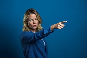 Lifestyle portrait photography of a glad girl in her 30s pointing down against a sapphire blue background. With generative AI technology