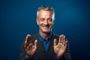 Medium shot portrait photography of a satisfied mature man joining palms in a gesture of gratitude against a sapphire blue background. With generative AI technology