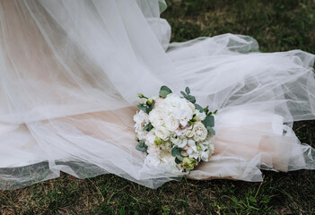 A beautiful bouquet of flowers, roses lies on a white dress with a long veil. Close-up wedding...