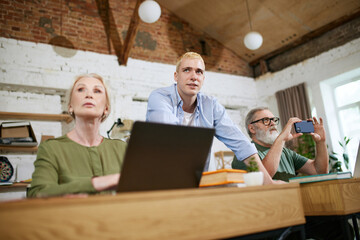 Fototapeta premium Business people, young guy and senior man and woman working together on project, having online meeting with colleagues. Concept of business, age, education, modernity, innovations, assistance