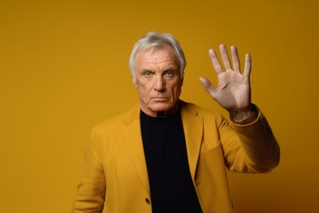Medium shot portrait photography of a tender mature man making a no or stop gesture with the extended palm against a gold background. With generative AI technology