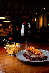surf and turf close-up with thick slice of sirloin steak and prawns with blackberry jam with red wine and blurred background
