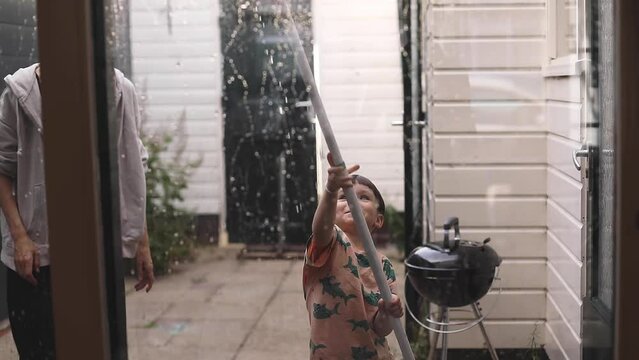 Cleaning little boy with mom washing windows using a squeegee to wash a window. Domestic work and household duties concept. Son help his mom wash window.