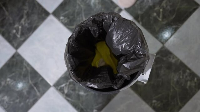 Closeup yellow sponge and gloves falling inside garbage bag in trash can. Close-up top view throwing away litter indoors after cleaning