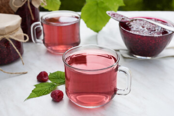 Fresh raspberry tea, berries and jars of jam on marble table. Vitamin C drink on white background. Anti-cold tea is an antioxidant for health in the flu season of colds. Side view.