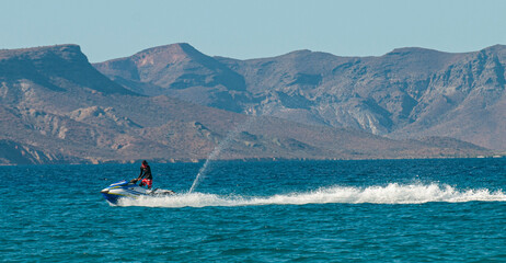 A guy on jet ski having fun in front of El Tecolote beach. In the background the isla Espiritu Santo on a sunny afternoon with blue sea and clear sky. La Paz Baja Mexico. - obrazy, fototapety, plakaty