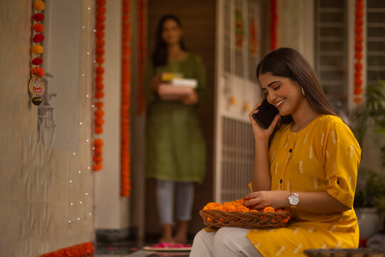 Young woman talking on mobile phone while decorating house with flower on the occasion of Diwali