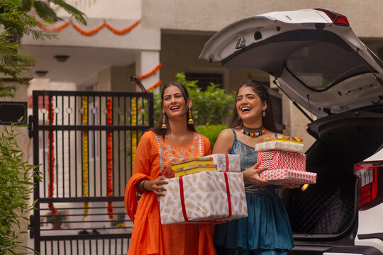 Two sisters unloading Diwali gifts from car trunk after shopping