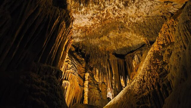 An underground cave formed of carbonate limestone rocks in Majorca, Spain. A colourful natural scenery in a cave with ancient cavities of stalactites and stalagmites on Mallorca, Balearic Islands.