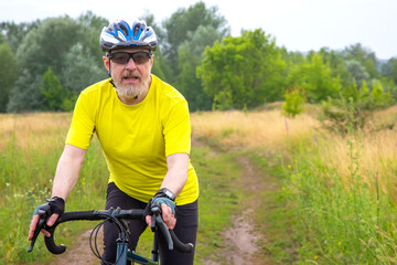 bearded man cyclist in yellow clothes rides a bike on a road in nature. sports, hobbies and entertainment for health