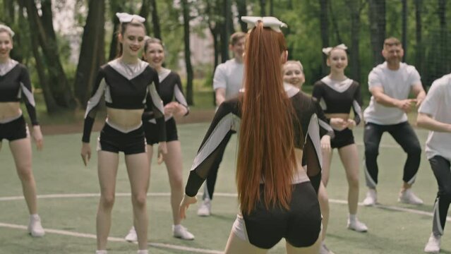 Group of young male and female cheerleaders doing squats while exercising with coach on soccer fieldGroup of young male and female cheerleaders doing squats while exercising with coach on soccer field