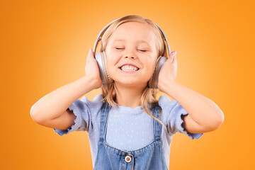 Headphones, smile or child streaming music to relax with freedom in studio on orange background. Face, singing or happy girl singer listening to a radio song, sound or audio on an online subscription