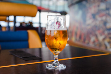 A beer in Tulip glass. Glass of light beer on wooden table in cafe or restaurant .Beautiful crystal glass with golden freshly brewed cold wheat beer stands on table cafe,restaurant terrace.
