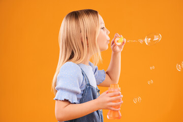 Girl, child and blowing bubbles in studio for fun, games and childhood development on mockup orange...
