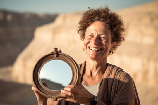 Close-up portrait photography of a joyful mature woman holding a mirror wearing a comfortable yoga top at the masada in southern district israel. With generative AI technology