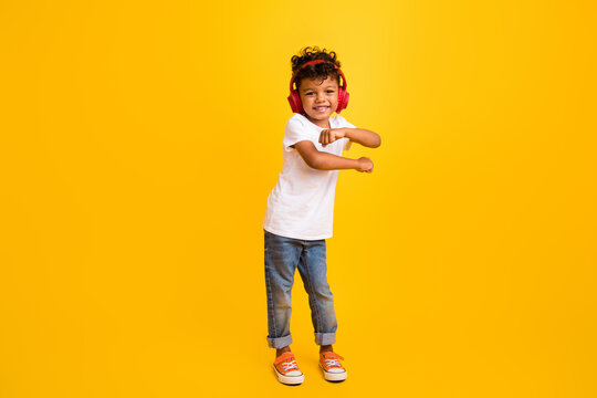 Full length photo of adorable pretty small boy wear white t-shirt dancing listening music headphones isolated yellow color background - Powered by Adobe