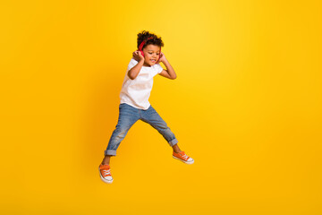 Fototapeta na wymiar Full length photo of excited funky small boy wear white t-shirt jumping high listening headphones modern device isolated yellow color background