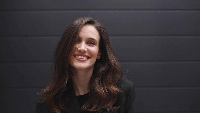 Close up of smiling girl looking at camera. Curly hair fashion model face smiling. Portrait of joyful girl shrugging her shoulder. Lovely coquettish brunette woman, winking playfully, flirting