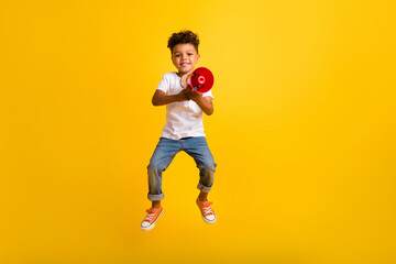 Full length photo of cute pretty small boy wear white t-shirt jumping high screaming bullhorn isolated yellow color background