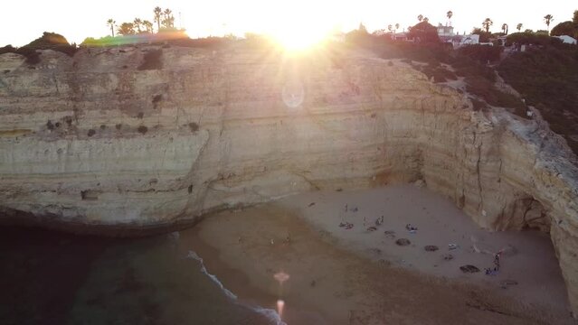 Aerial Landscape Reverse Movement of Beach with Sun Rays Peaking Through. A bird's eye view of the beach, ocean, and people with a movement backwards.