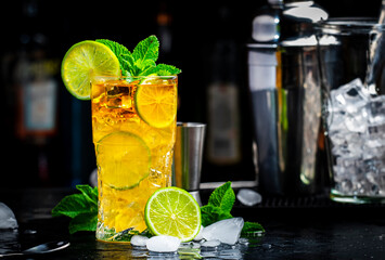 Dark and Stormy cocktail drink with dark rum, ginger ale, lime and ice with bottles, black bar counter background