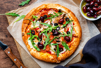 Homemade Pizza with sausage, cheese, mushrooms, olives, tomato sauce and arugula, rustic wooden table background, top view