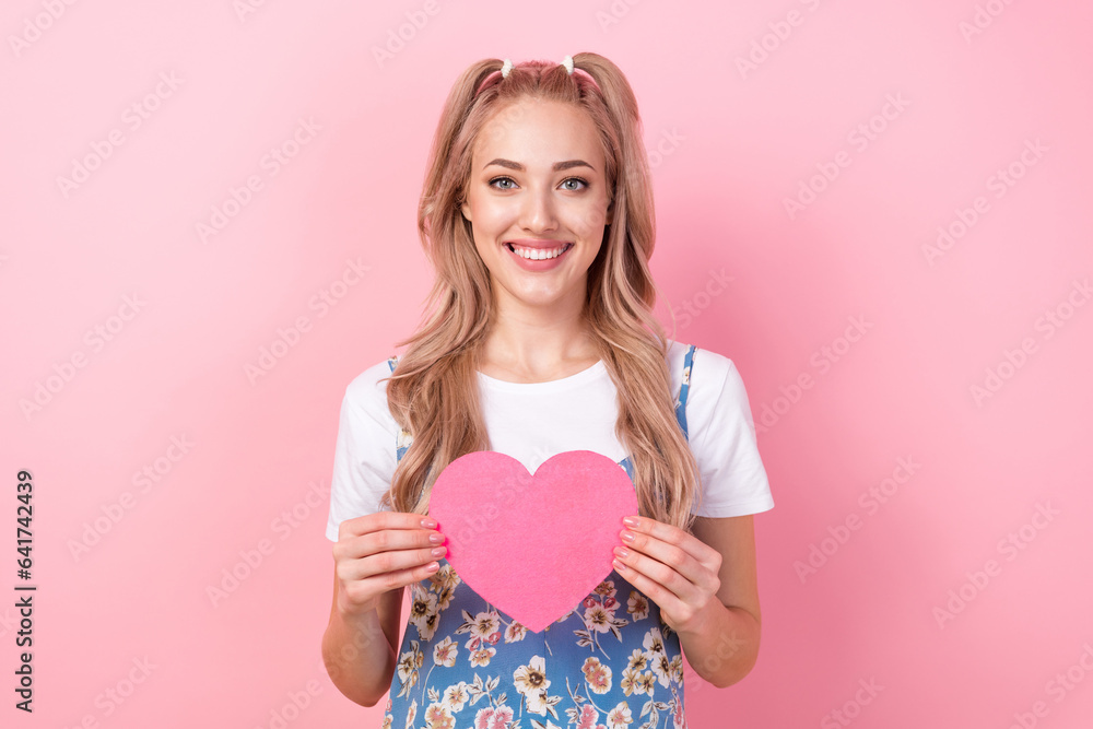 Sticker Portrait of toothy beaming girl with tails wear t-shirt under dress fingers hold paper heart postcard isolated on pink color background