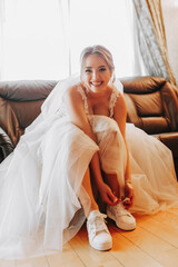 Happy bride ties sneakers and looks into camera lens. Preparing the bride for the ceremony....