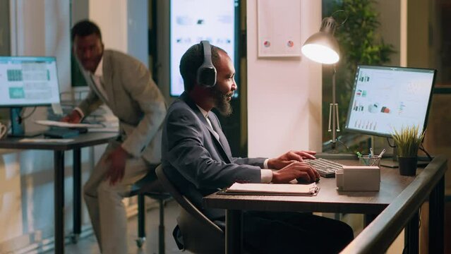 Management executive interrupting worker listening to music slacking in office to show him mistake he needs to fix. Employee taking headphones off after being given tasks to do by supervisor