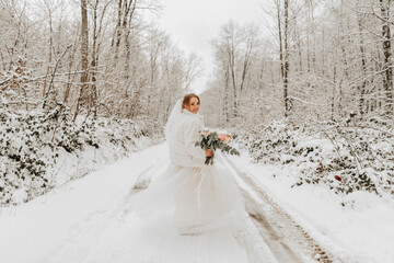 A beautiful bride in white is walking down the road in a fabulous snowy winter forest. Portrait of...