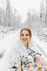 A beautiful bride in a white dress with a bouquet of flowers in a fabulous snowy winter forest. Portrait of the bride in nature.