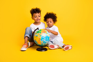 Full body portrait of cute intelligent curious brothers sit floor look planet earth globe isolated on yellow color background