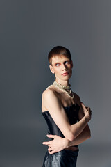queer person in black corset and pearl necklace posing on grey backdrop, edgy fashion, makeup