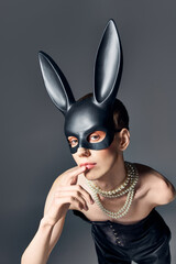 queer person in corset and bdsm bunny mask posing on grey, finger near lips, fashion, look at camera