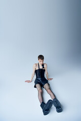 queer person in black corset and fishnet tights sitting on grey, androgynous model, lgbt fashion