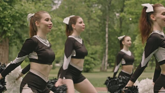Cheerleading squad in uniform dancing with pom-poms during performance on outdoor sports field