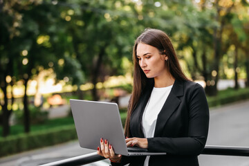 
Happy young business woman typing on a laptop. A woman in a suit is satisfied with her work and a successful deal.