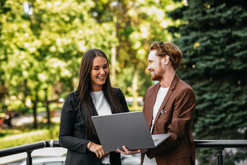A handsome red-haired man and a brunette in business suits on a summer terrace. Senior entrepreneurs at a business meeting in an outdoor restaurant are discussing a project on a laptop.