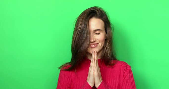 Smiling peaceful young woman practicing yoga and meditation. Calm woman making Namaste gesture and looking at camera. Young spiritual woman praying gesture isolated on green background. Thankful girl.