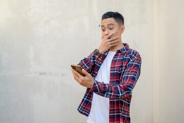 Indonesian man wear casual clothes surprised when looking the smartphone. The photo is suitable to use for man expression advertising and fashion life style.