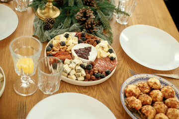 Modern christmas cheese platter with cranberry sauce as christmas tree, fir branches and pine cones, candles, appetizers, glasses and cutlery. Food arrangement for holidays. Christmas table setting