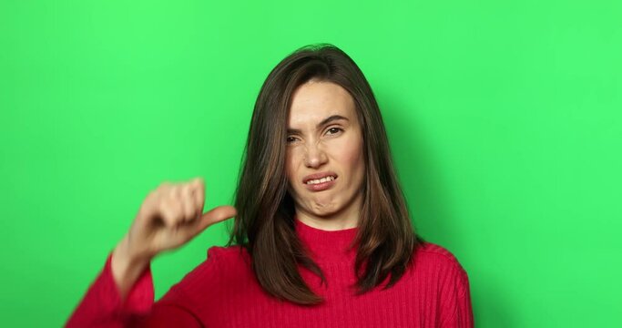 Displeased brunette young woman posing isolated on green background studio.Girl looking camera say no with finger gesture showing thumb down and showing tongue.