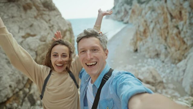 happy lovely couple young smiling woman and mid aged man hiking rocky canyon at seaside and taking selfie. wanderlust and travel summer vacation trip. using phone camera for filming