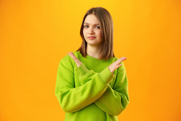 Teen girl shows cross hands gesture, rejecting something over yellow background in studio