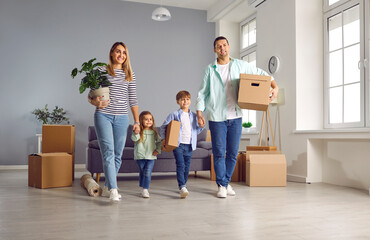 Happy family with two kids on moving day smiling with unpacked boxes and plant in hands in their new apartment. Home owners enjoying buying flat. Relocating, real estate, mortgage concept.