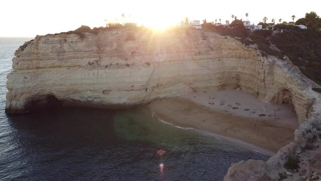 Aerial Landscape Sandy Beach and Ocean with Sun Leaks. Pan left slowly from beach to ocean and rock bolder with the sunbeams peeking through.