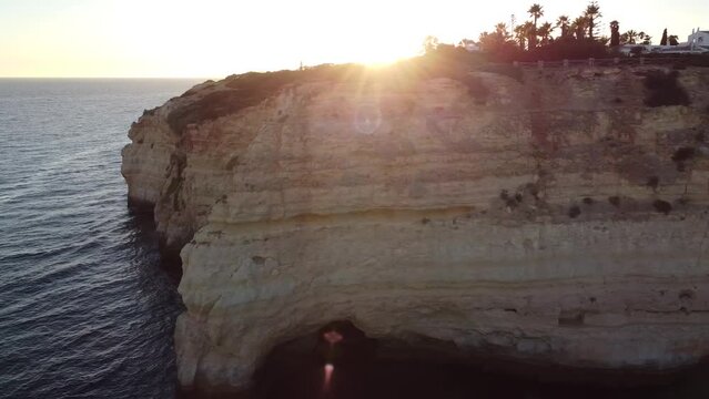 Aerial Drone Horizontal View with Sunset Sun Beams Leaking Through. Right pan towards beach with scene of ocean, beach, rocks, and people enjoying the beautiful sunny and sandy beach. 