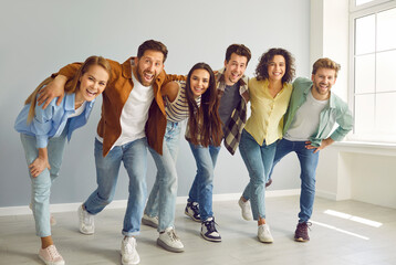 Portrait of a group of happy smiling funny friends students or colleagues in casual clothes standing together and laughing isolated on a gray background and looking positively at the camera.